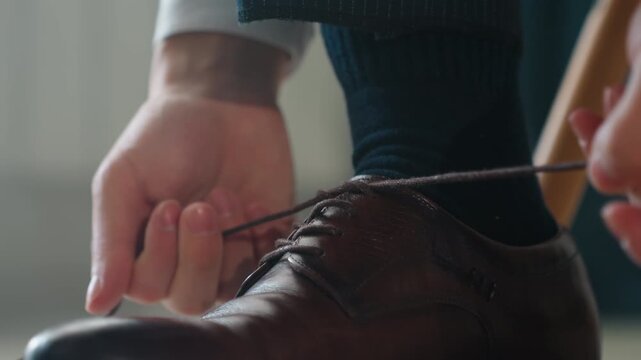 White man closeup hands tying shoelace detailed fingers knotting lace, intimate shallow depth, textured leather, blue sock, patient ritual before wedding or ceremony, precise motion and focused
