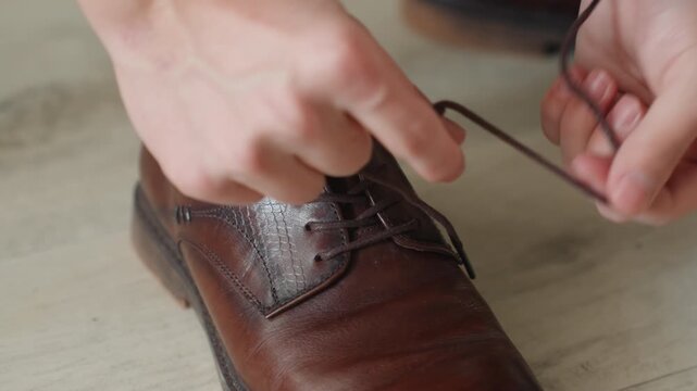 Hands tying brown leather shoe, closeup of man preparing for formal event, careful knotting of lace, textured polish on vintage oxford, calm morning atmosphere with fingers adjusting sock