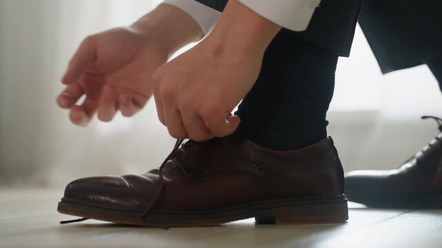 White man hurriedly lacing brown dress shoe, closeup fingers pulling lace with tense motion, briefcase ready commuter racing to office, alarm triggered routine, knotting for fast departure, urban