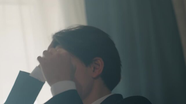 Asian businessman adjusting hair by window, suit clad executive preparing meeting, soft backlight silhouette, hands smoothing hair, subtle nervous energy, muted cinematic tones, morning daylight
