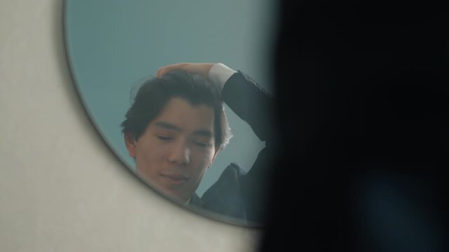 Asian man in suit checking reflection in round mirror framed by silhouette of coat, soft morning light, final hair touch and subtle smile, poised commuter energy ready for business meeting