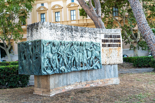 Bari, Italy - June 31, 2026: Bronze relief sculpture depicting historical scene of figures and cart mounted on stone pedestal in public park near historic building