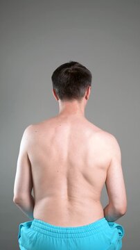 Unrecognizable man performs exercises for muscles of upper back, arms and shoulder joint. Posture correction and physical therapy on gray background