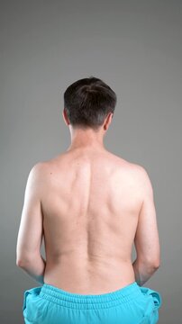 Unrecognizable man performs exercises for muscles of upper back, arms and shoulder joint. Posture correction and physical therapy on gray background