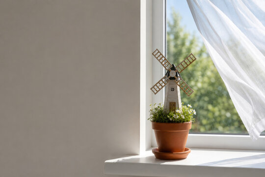 Miniature windmill stands in flower pot by window. Space for text.