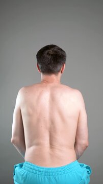 Unrecognizable man performs exercises for muscles of upper back, arms and shoulder joint. Posture correction and physical therapy on gray background