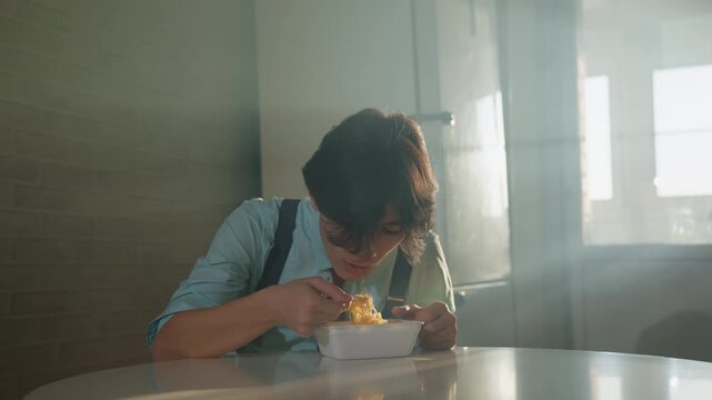 Casual man savoring noodles during day. Lively midday cafe scene with cheerful man and warm sunlight. Relaxed Asian man indulging in noodles amid lively city cafe atmosphere with gentle light
