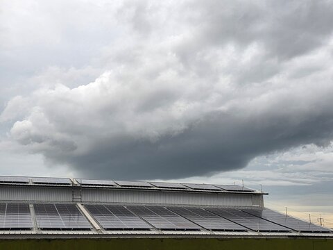Solar Power Infrastructure under Stormy Sky: Rows of solar panels installed on a rooftop reflect the dramatic, dark clouds of an approaching storm.