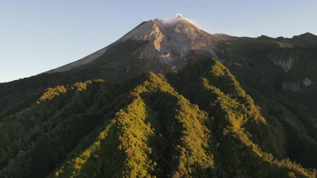 Aerial Footage of Mount Merapi Volcano with Lush Forested Slopes and Its Peak Illuminated by Golden Sunrise Under a Clear Sky. Majestic Volcanic Landscape in Yogyakarta, Indonesia.