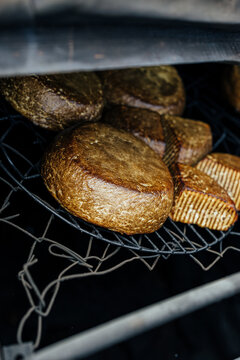 Two wheels of homemade smoked goat cheese resting on a metal rack inside a rustic outdoor smoker, showing a dark golden rind and traditional artisanal preparation