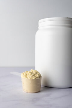 Protein powder in a scoop with container on a light surface 