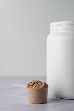 Protein powder in a scoop with container on a light surface 