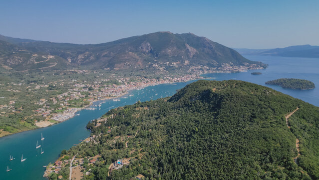 High aerial view of Nydri bay surrounded by green hills with yachts anchored in calm water and Skorpios island in background on Lefkada island Greece for travel stock