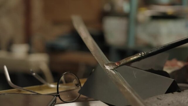 Elderly craftsman working in his old workshop, carefully restoring collectible Japanese bladed weapons
