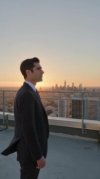 Side view of a thoughtful businessman standing on the rooftop of a skyscraper looking over the big city at sunset