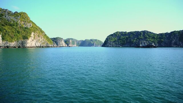 A panoramic daytime view of steep limestone karsts and jungle-covered islands rising from calm blue-green waters in Halong Bay near Cat Ba Island Vietnam.