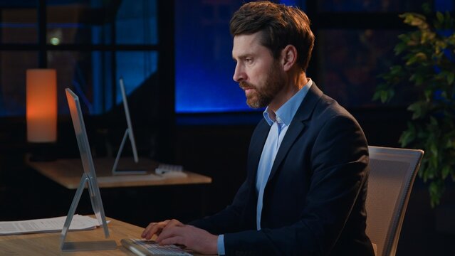 Serious concentrated adult Caucasian business man working with computer at late night evening in office workplace businessman male executive boss work busy with online job startup project overworked
