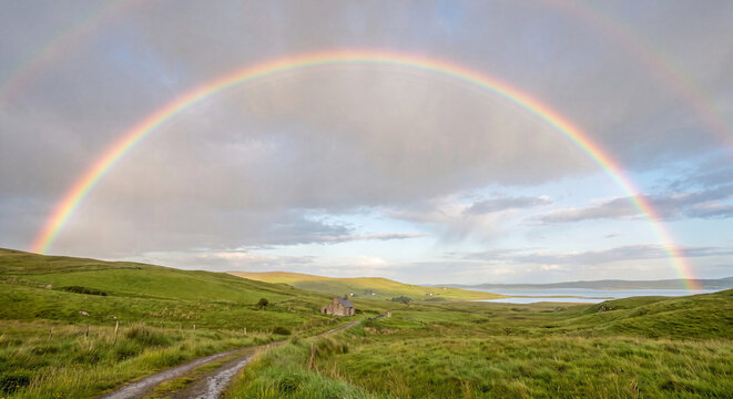 Rainbow over rolling green hills and winding path beneath a cloudy countryside sky