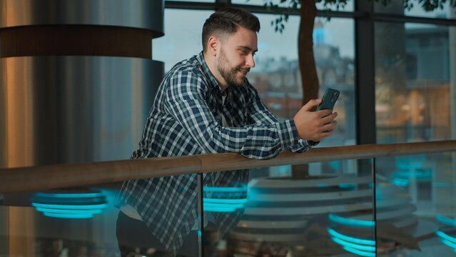 Smiling Caucasian man using mobile phone app happy messaging with device watch funny web content looking in cellphone client scrolling social media in shopping mall wi-fi male guy use smartphone smile