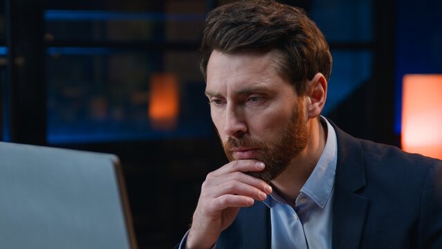 Concentrated Caucasian middle-aged business man working with computer thinking at evening pensive looking in desktop monitor adult mature male businessman company owner thoughtful work at night office