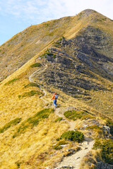 Fototapeta premium Hiker ascending trail toward summit Talijanka in Accursed Mountains, two distant figures visible higher on slope. Shows human scale within expansive mountain scenery and valuing the journey itself.