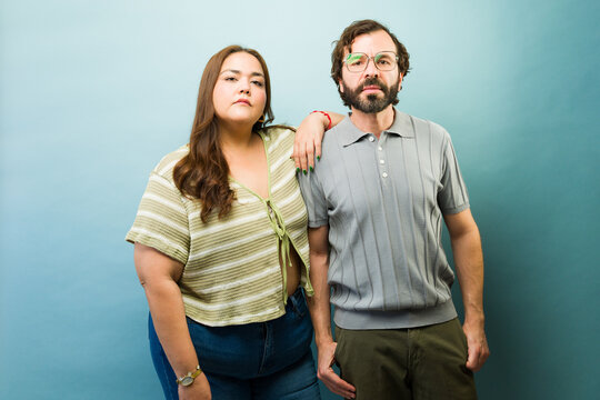 Portrait of diverse adult couple standing confident and serious against blue background expressing partnership and modern lifestyle