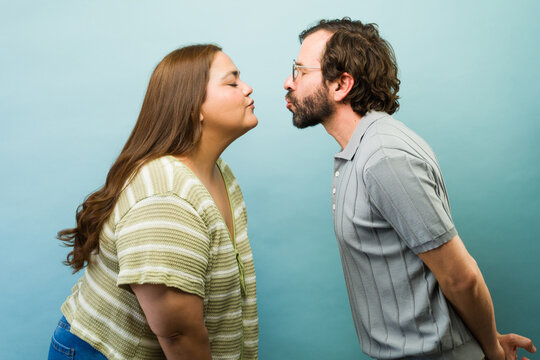 Romantic couple making kissing face in profile against a blue background, expressing love and affection