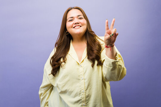 Body positive woman showing peace sign, smiling cheerfully and feeling happy with her confident attitude