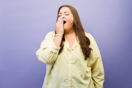 Woman yawns, covering her open mouth with her hand against a purple background, looking tired and sleepy