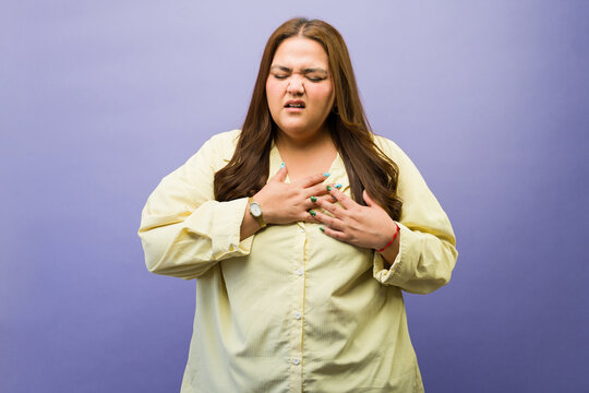 Hispanic woman feeling severe chest pain and breath shortness, holding hands over her heart due to an urgent medical condition