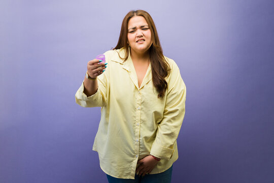 Confused woman holding menstrual cup feeling uncertain about feminine hygiene product against purple background