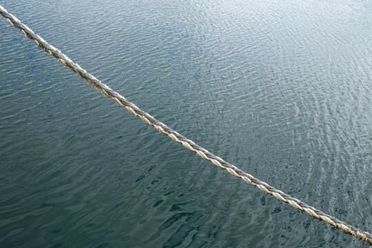 Thick mooring rope keeps a boat secured to the stone pier at Buckie Harbour in Moray, Scotland, during a calm and bright afternoon on the water