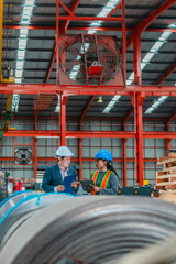 Naklejka premium Manager and female worker discussing over clipboard among steel coils in warehouse factory