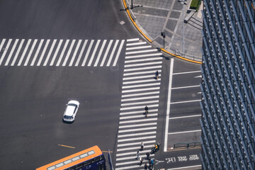 Fototapeta premium Overhead view of a rounded office forecourt where crossings meet a busy carriageway, shadow from the tower cutting diagonally across the paved corner, documenting downtown commuter flow.
