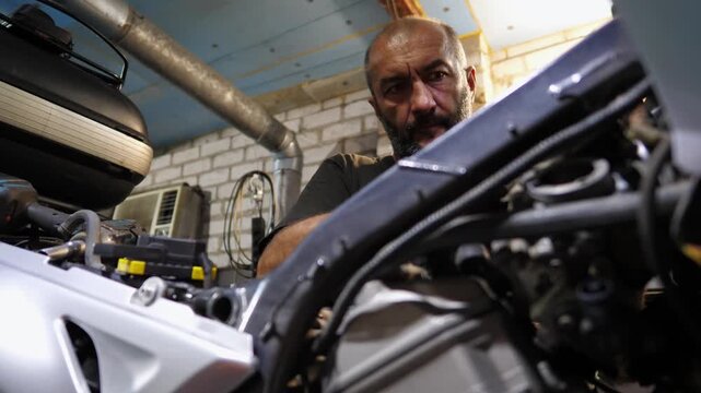 Male repairer fixing motor of motorbike using tool at workplace. Professional mechanic repairing engine of motorcycle at workshop. Adult repairman working at garage. Concept of maintenance service