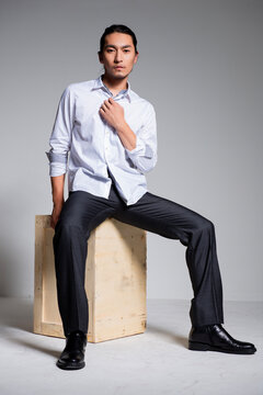 Asian sexy man wearing a white shirt and suit pants against a gray background