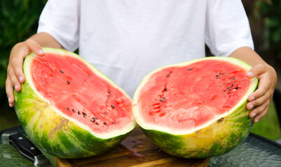 Smiling boy holding a freshly cut watermelon half at an outdoor garden table © Olena Smerichka