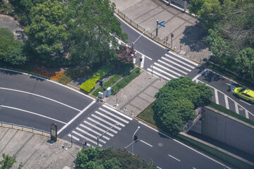 Obraz premium Aerial view of pedestrian crossings beside a landscaped road underpass ramp, flowering beds edging the descent into the underpass, a study in street geometry and lane use.