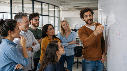 Obraz premium Group of diverse professionals engaged in a brainstorming session, with a man presenting ideas on a whiteboard in a modern office environment filled with natural light and collaborative workspace