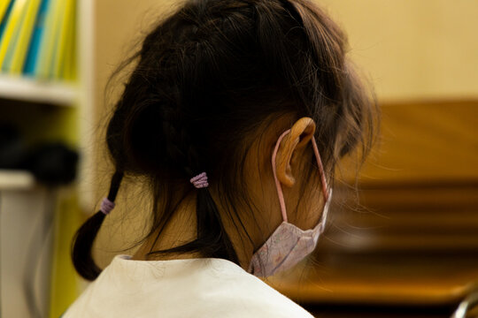Child wears mask and has hair in braids while sitting in classroom in afternoon light