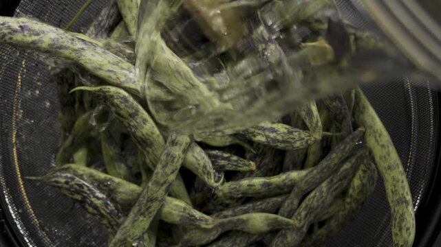 Washing green bean pods with pouring water inside colander top view, 4K