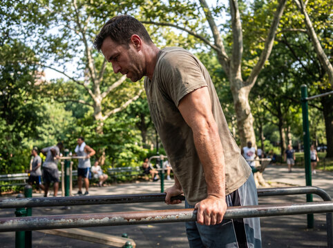 Athlete performs intense tricep dips on parallel bars at an outdoor public park during a sunny afternoon training session to improve upper body strength.