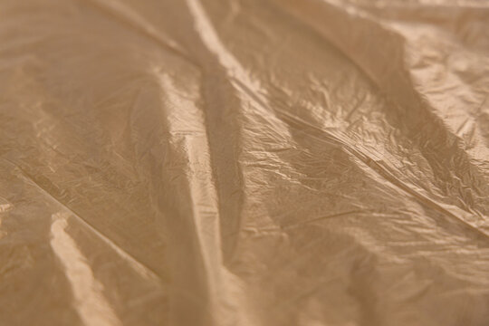 Close-up view of crumpled and shiny beige plastic sheet on a flat surface
