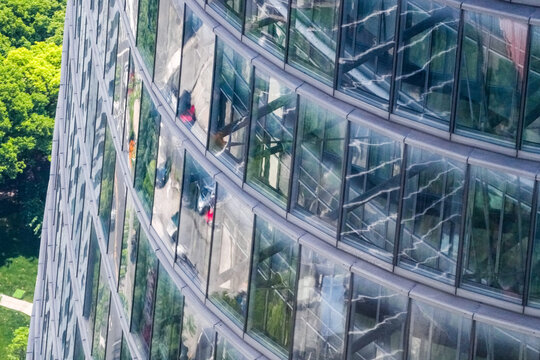 Aerial close view of a curved glass tower facade with occupied floors visible behind the glazing, reflections of the district sliding across the curved glass, high above the daily commute.