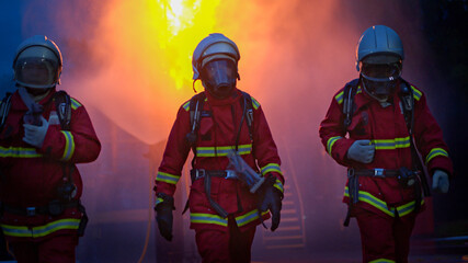 Naklejka premium The four firefighters in protective gear walk through the remaining smoke and flames after completing an emergency response operation to extinguish a fire inside an industrial plant
