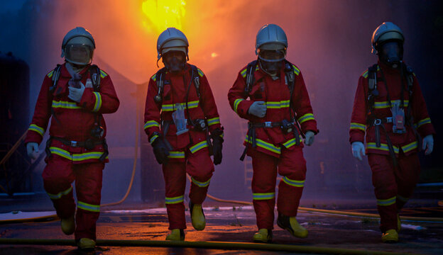 The four firefighters in protective gear walk through the remaining smoke and flames after completing an emergency response operation to extinguish a fire inside an industrial plant