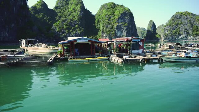 A coastal fishing village with wooden docks and colorful stalls nestled in a sheltered bay surrounded by towering limestone karsts on Cat Ba Island, Vietnam.