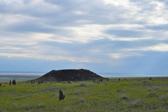 Ancient Besshatyr kurgan burial mound complex in Altyn-Emel National Park. Sacral archaeological site with stone menhirs, burial mounds and distant mountains under a blue summer sky.