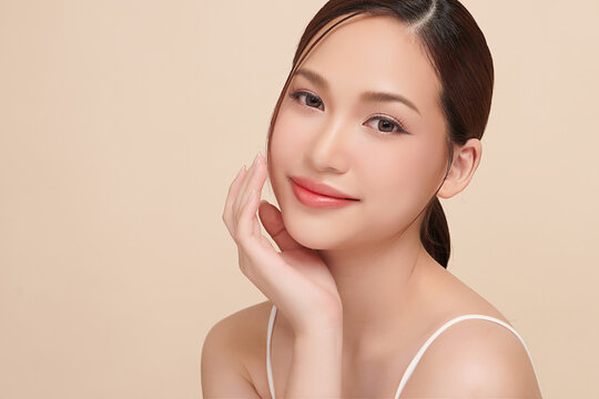A beautiful young Asian woman with clean, fresh skin against a beige background. Skincare, facial treatment, cosmetology, beauty, and spa. An elegant portrait of an Asian woman.
