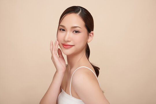 A beautiful young Asian woman with clean, fresh skin against a beige background. Skincare, facial treatment, cosmetology, beauty, and spa. An elegant portrait of an Asian woman.